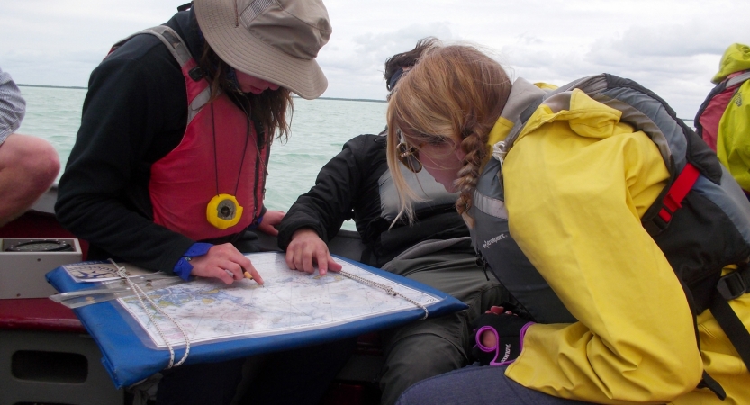 Three people sitting in a sailboat examine a map.
